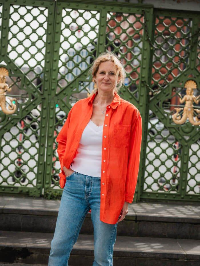 woman wearing red linen shirt and jeans in front of iron gates